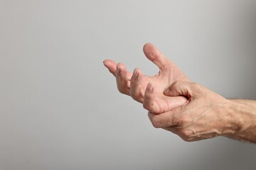 Arthritis symptoms. Man suffering from pain in hand on gray background, closeup. Space for text
