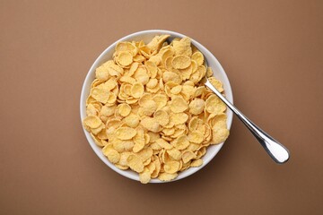 Breakfast cereal. Tasty corn flakes in bowl and spoon on brown table, top view