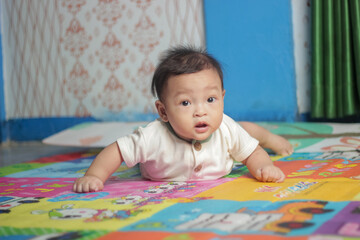 Cute asian baby boy lying on her stomach on mattress learning to crawl.