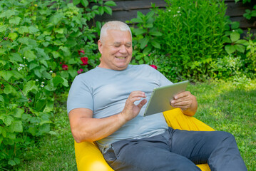elderly man using a tablet while relaxing in the garden - 749674632