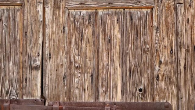 An old wooden door with a hinged vintage iron bolt. Rusty massive iron lock on an abandoned wooden gate. Sun-faded, aged and bark beetle-eaten wooden doors. Rovinj, Croatia - February 29, 2024