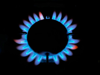 A blue flame burning on a gas burner on a kitchen stove in the dark