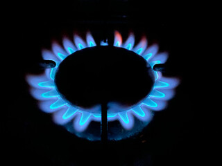 A blue flame burning on a gas burner on a kitchen stove in the dark
