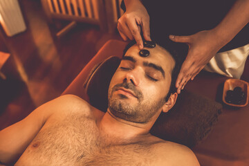 Caucasian man enjoying relaxing anti-stress head massage with hot stone and pampering facial beauty...