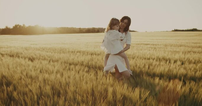 young mother and daughter together happily walking on sunny wheat meadow hugging smiling. mother carries her daughter in arms, gently presses to her and kisses. Future of Ukraine. calm Peaceful life
