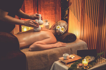 Hot herbal ball spa massage body treatment, masseur gently compresses herb bag on woman body....