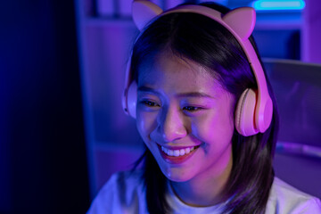 A beautiful female gamer happily plays in a private room with dim lighting that is perfect for...