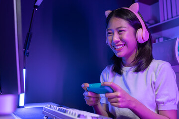 A beautiful female gamer happily plays in a private room with dim lighting that is perfect for...
