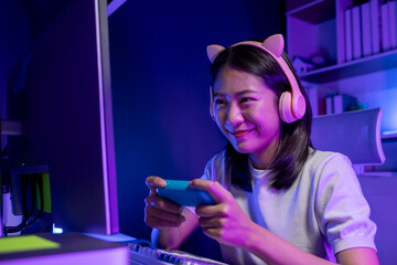 A beautiful female gamer happily plays in a private room with dim lighting that is perfect for...