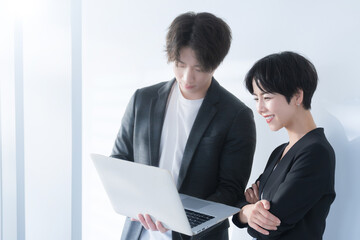 逆光の中パソコンを持った笑顔のビジネスウーマンとビジネスマンの上半身のコピスペースあり　資料を一緒に見るなどの会話のイメージ 