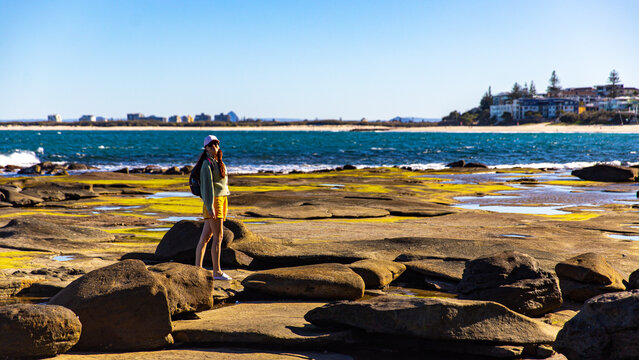 pretty girl enjoying a sunny day on the beach in caloundra, sunshine coast, queensland, australia; exploring rock pools on the shore of pacific ocean near brisbane