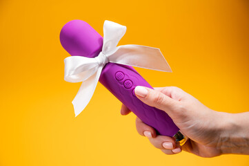 Woman holding purple vibrator with white bow on orange background. 