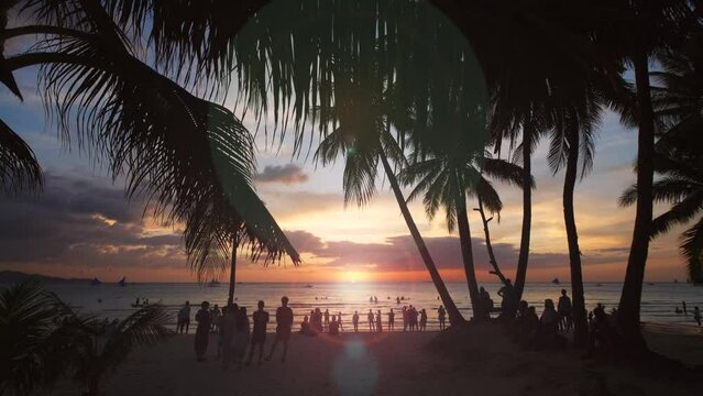 Silhouetted people and palms near sea. Sunset at tropical White beach, Boracay island, Philippines, slow motion 4k