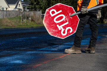 Traffic control worker in orange reflective safety vest with temporary stop sign managing traffic...
