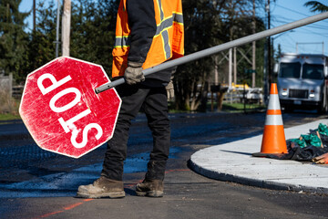 Traffic control worker in orange reflective safety vest with temporary stop sign managing traffic in a road work construction zone
