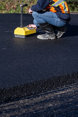 Road construction, technician testing freshly laid asphalt compaction with a nuclear density gauge...