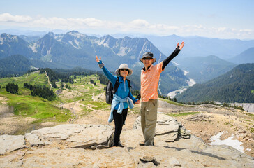 Couple raising arms at Skyline Trail. High mountains in the background. Mt Rainier National Park. Washington State.
