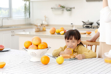 Asian daughter drinking freshly squeezed orange juice in the kitchen