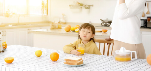 Asian daughter drinking freshly squeezed orange juice in the kitchen