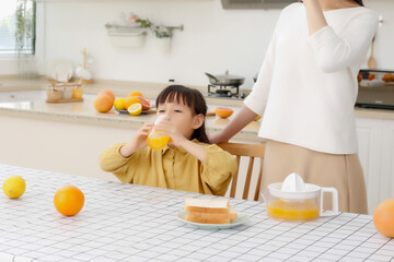 Asian mother drinking freshly squeezed orange juice with her daughter in the kitchen