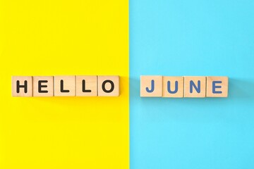 Hello month of June concept. Wooden blocks typography in bright blue and yellow background.	