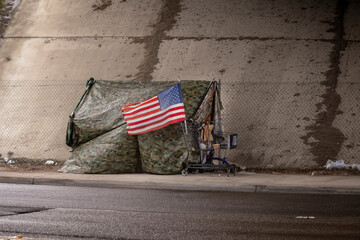 An American flag at a homeless tent made of camouflage tarp at a road underpass