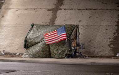An American flag at a homeless tent made of camouflage tarp at a road underpass