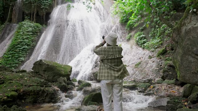A woman photographs a waterfall in a tropical rainforest