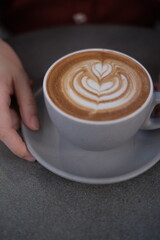 Cup of coffee latte with heart shape in cafe  in coffee shop with hand 