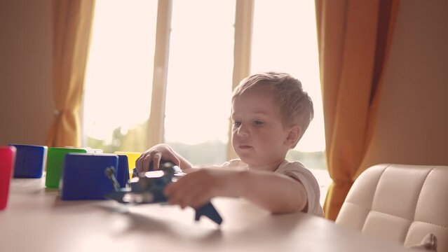 child baby playing with toys airplane car. happy family kid dream concept. child son on the table near the window plays a toy plane lifestyle car cubes the glare of the sun from the window