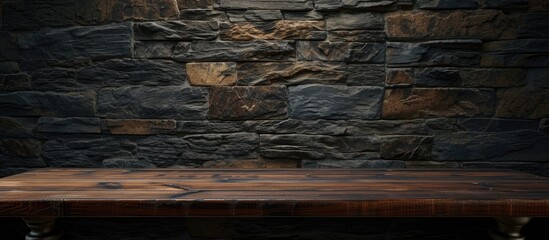 A wooden table is placed in front of a solid stone wall. The table appears to be empty, possibly in a coffee shop or restaurant setting, with a background suitable for product display or montage - obrazy, fototapety, plakaty