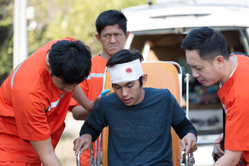 Injured man broken head and bandage on patient transport stretcher. Ambulance staff member assisting injured person. Paramedics assisting injured person first aid on road