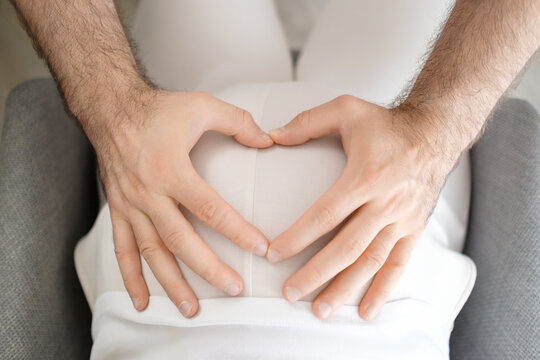 Mans hands make a shape of heart on the pregnant belly of woman