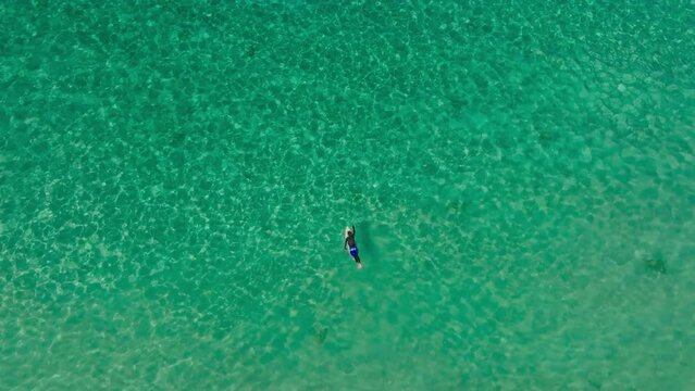 Aerial view of a surfer swimming with surfboard in the turquoise water
