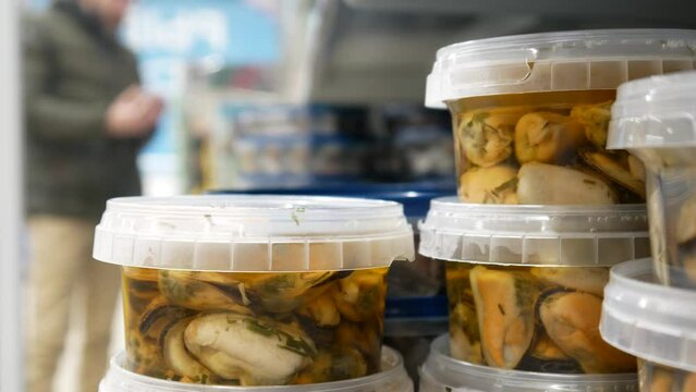 Close-up of many plastic containers with mussels in marinade and a man's hand takes one