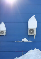 a snow-covered air conditioner on the wall of the building	