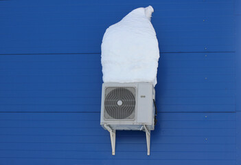 a snow-covered air conditioner on the wall of the building