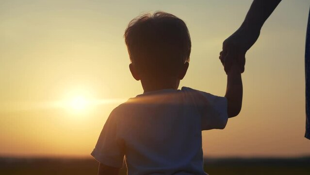 mom and son in the park. mom a holding her son hand walking in the park lifestyle silhouette at sunset in nature. happy family kid dream concept. mom and son family walking in nature