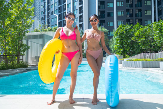 Female friends in bikinis playing with colorful rubber rings by the pool