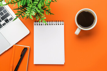 Flat lay blank notepad, cup of coffee, potted plant and laptop computer on orange background