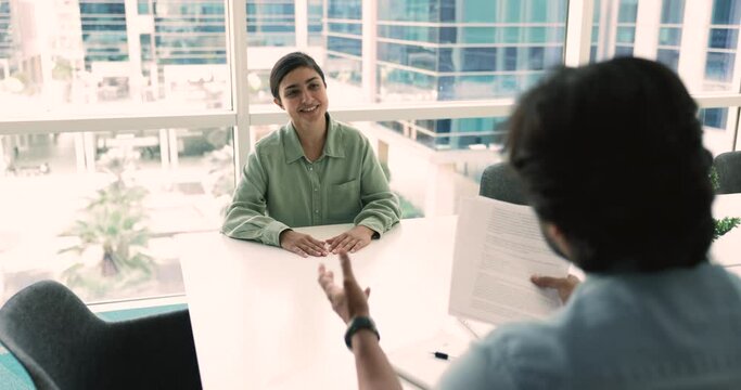 Pretty Indian woman pass job interview in company office, lead conversation with man HR manager holding resume ask about education, experience and skills to young female vacancy candidate in boardroom