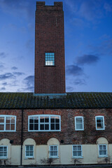Tall brick tower rising above a brick building against a dusky blue sky with clouds