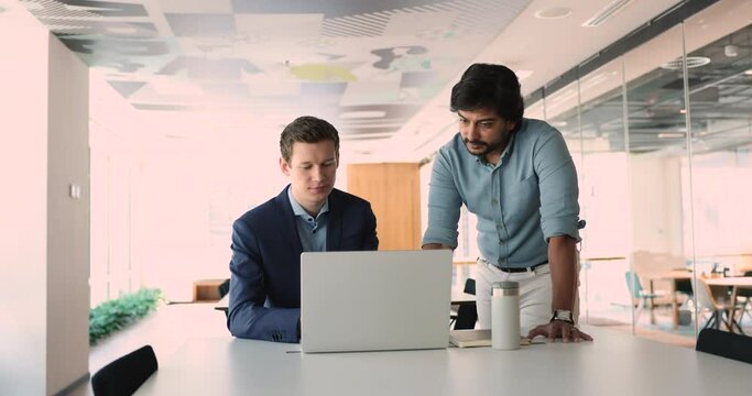 Corporate mentor teach intern, give advice, supervising work of newcomer met in coworking office. Multiethnic teammates using laptop at workplace, prepare task, discuss presentation or new application