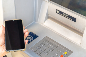 Older woman brings the phone to the ATM, NFC contactless communication concept