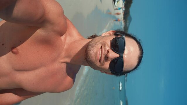 Man stands on beach holding phone looking at camera chatting with friends via video call. Beach vacation modern technology video call leisure time tropical scenery connected video call with friends.
