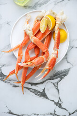 Boiled opilio or snow crab with lemon wedges, above view on a white marble background, vertical shot