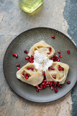 Manti served with pomegranate seeds and yogurt, vertical shot on a beige and grey granite background, elevated view