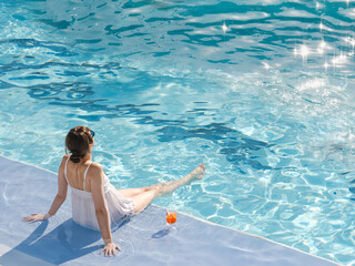 Cute woman with a glass of drink sits near the swimming pool of a cruise ship. Sunny, clear...