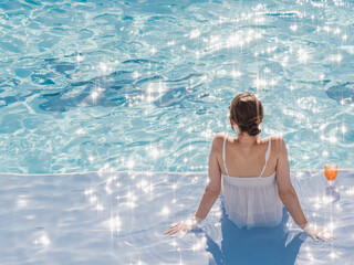 Cute woman with a glass of drink sits near the swimming pool of a cruise ship. Sunny, clear...