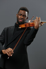 Elegant African American man in black suit playing violin on gray background in music performance...